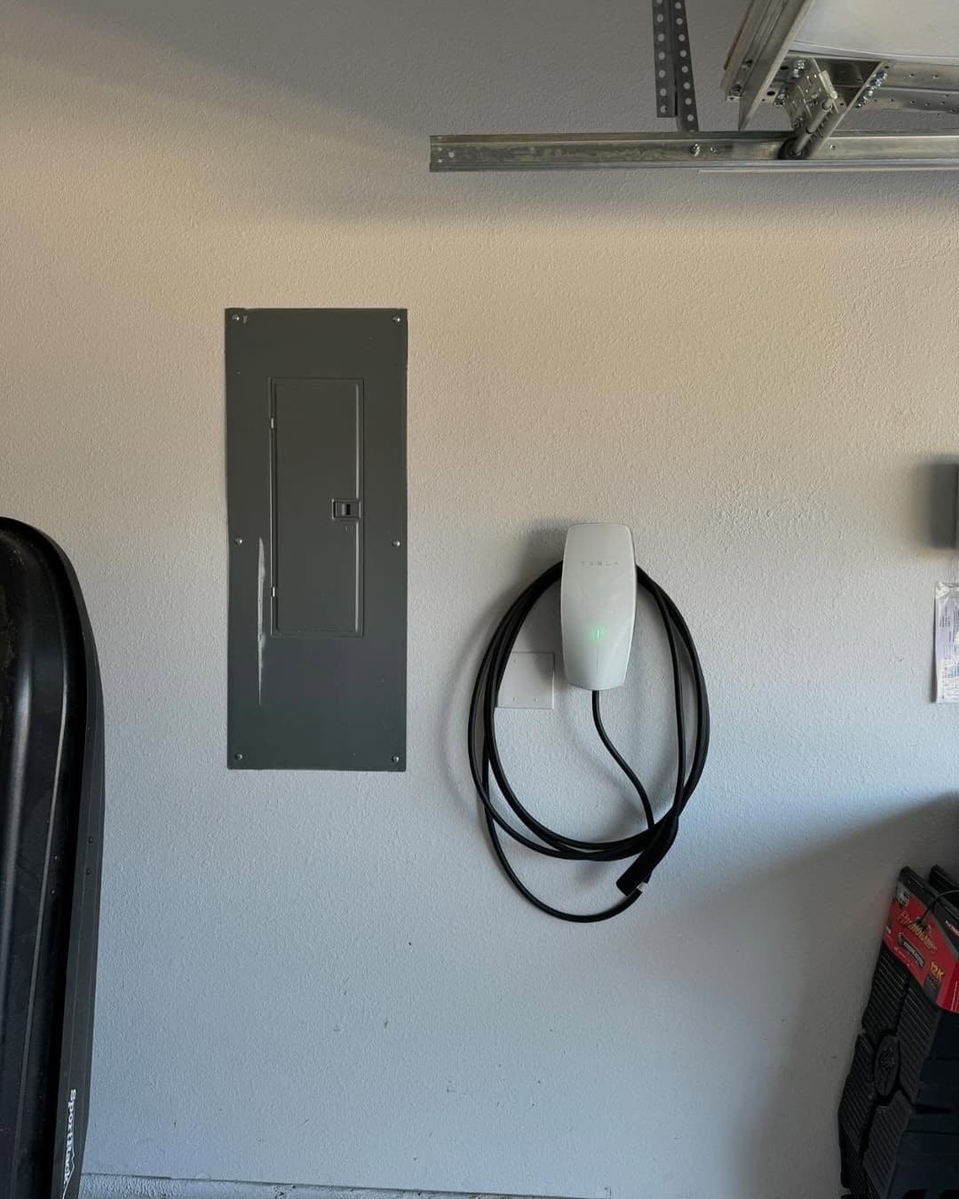Electric vehicle charger mounted on garage wall beside electrical panel. Charging cable neatly coiled.