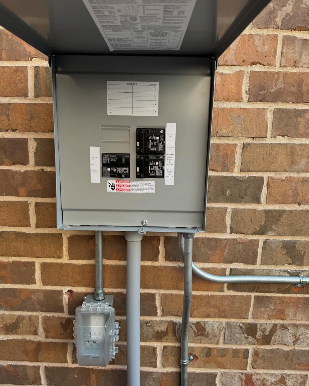 Electrical panel mounted on a brick wall with circuit breakers and a meter box.