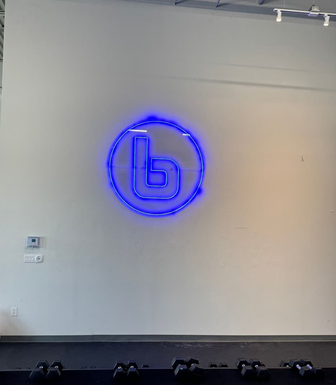Blue neon logo on a white wall, featuring a letter "b" in a circular design.