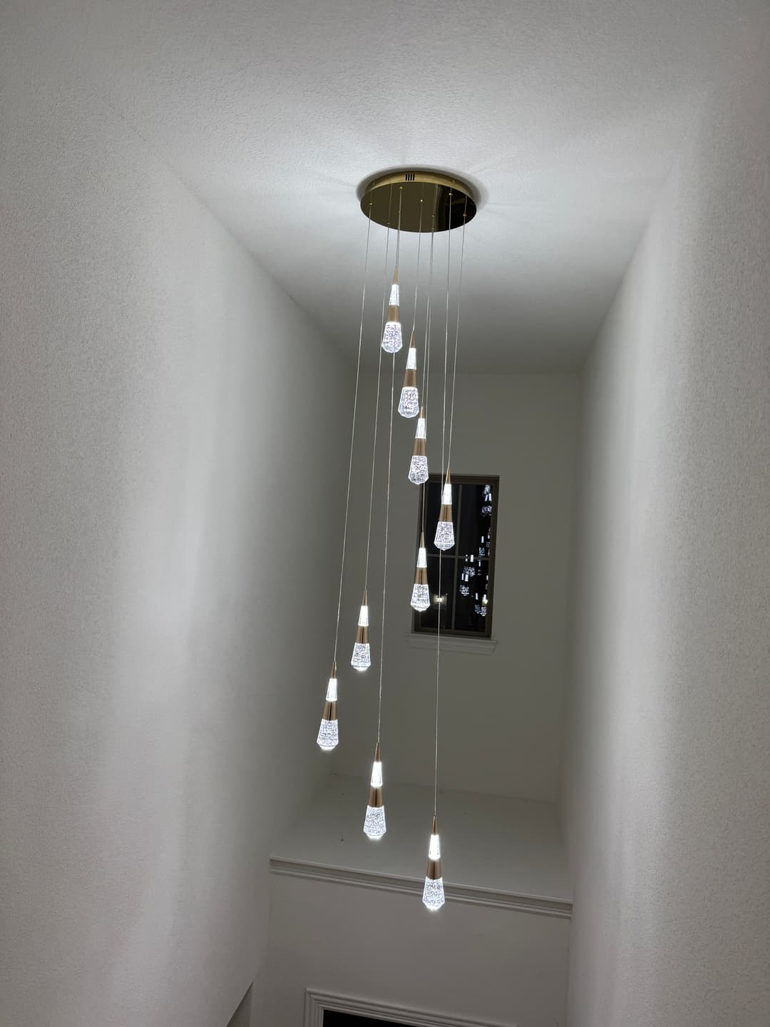 Modern pendant lighting fixture hanging in a hallway with multiple glass bulbs.