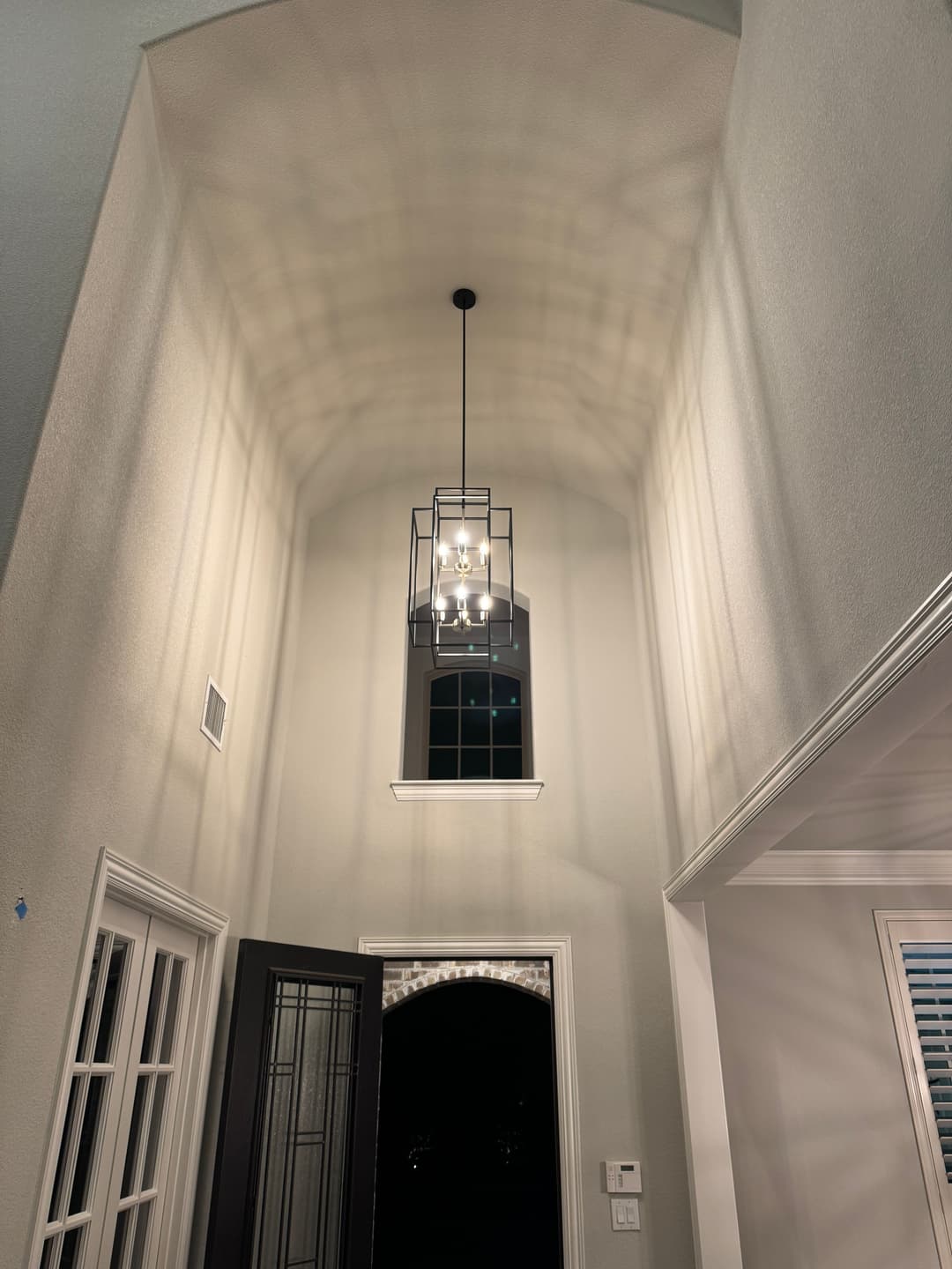 Elegant entryway with tall ceiling and stylish pendant lighting casting shadows.