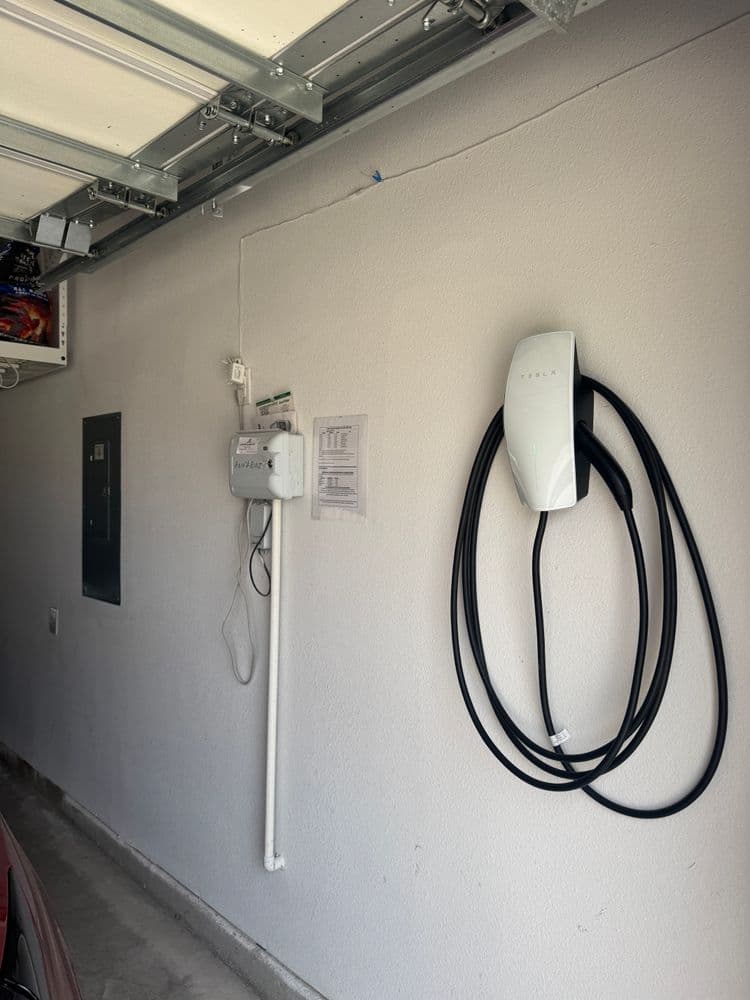 Tesla EV charger mounted on a garage wall with electric panel nearby and charging cable hanging.