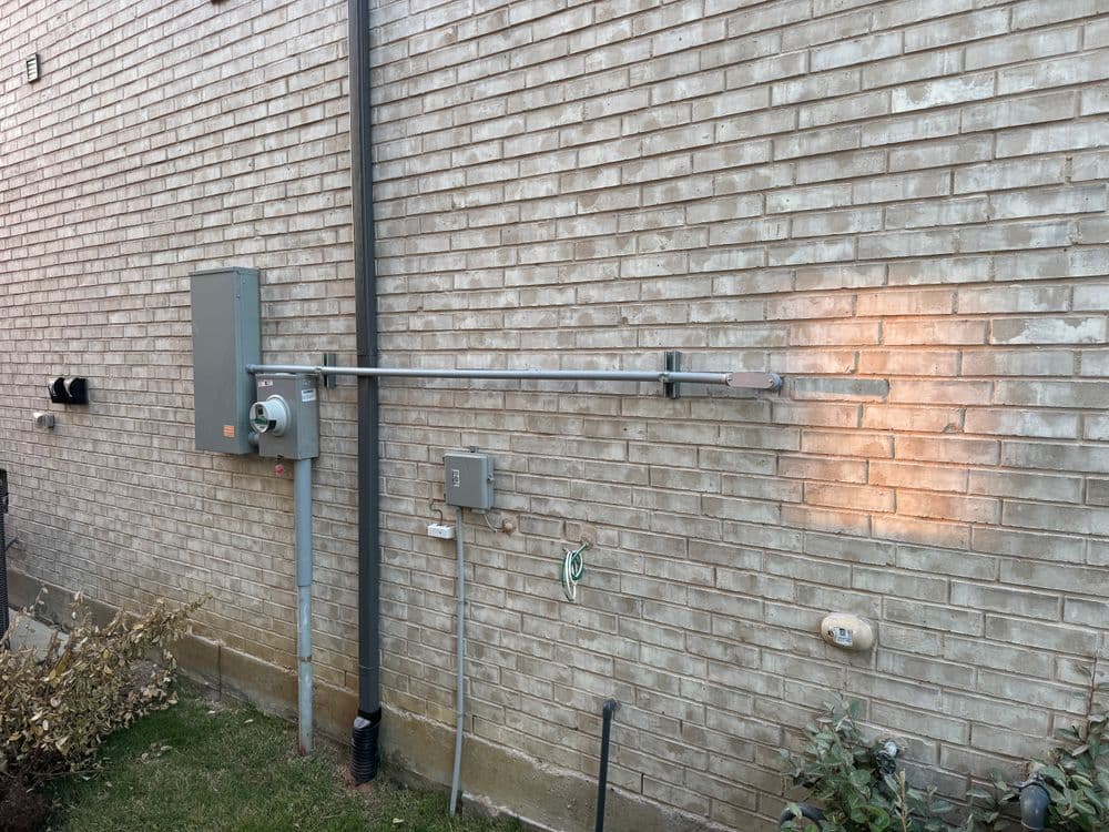 Electrical meter and disconnect on a brick wall, showcasing utility setup and outdoor wiring.