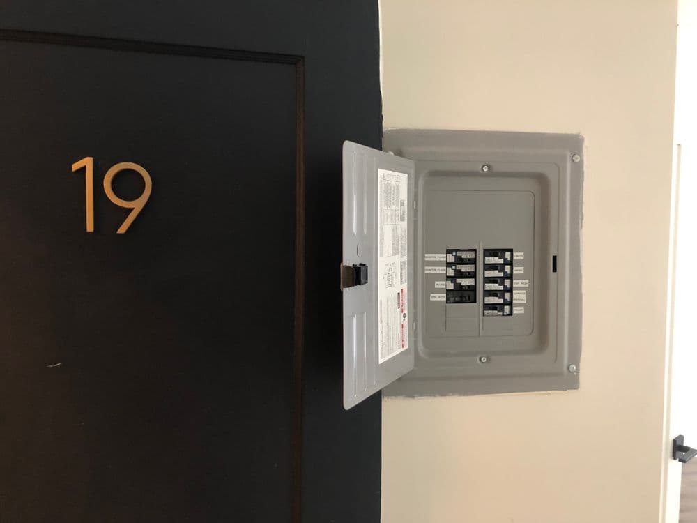 Electrical panel next to door number 19 in an apartment hallway.