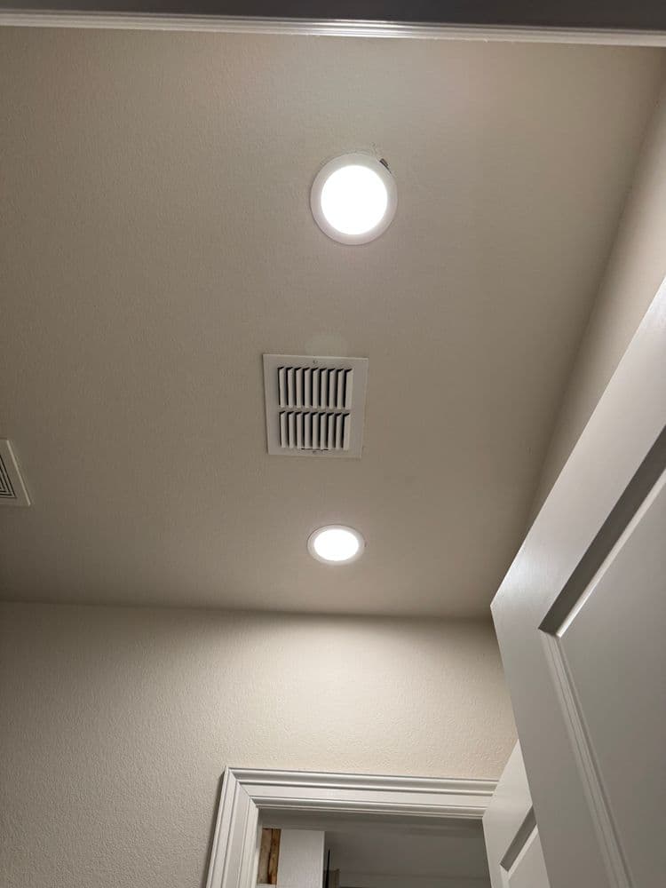 Ceiling lights and vent in a modern room with white walls and door frame.