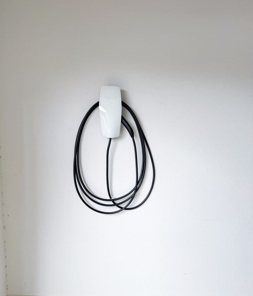 White cable holder with black cables neatly organized on a white wall.