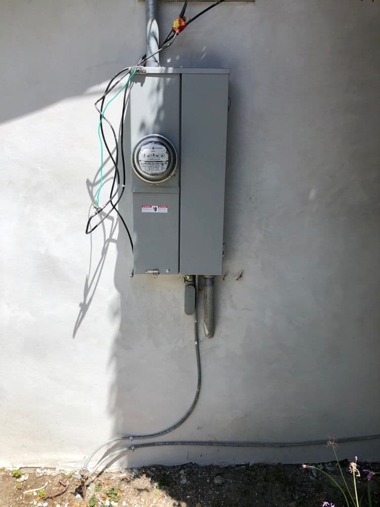 Electric meter mounted on a wall with wires and conduits. Important for home energy management.