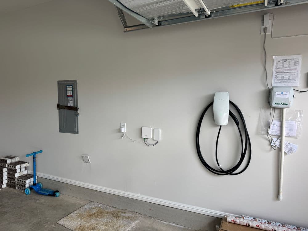 Garage interior with electrical panel, wall-mounted EV charger, and scooter.