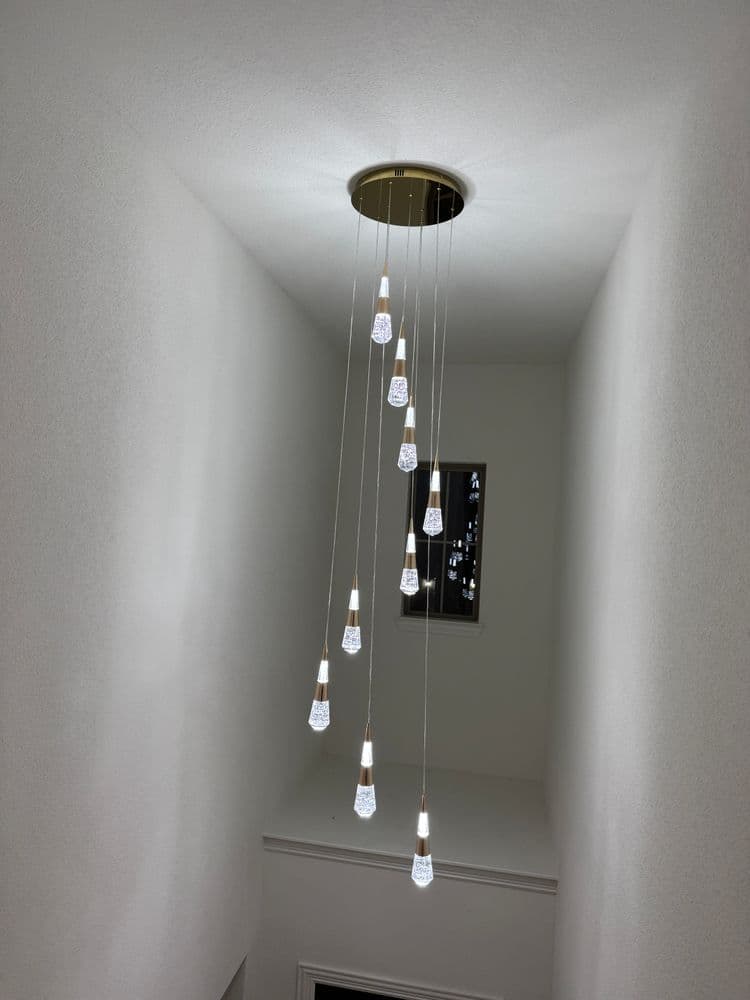 Modern chandelier with cascading glass lights illuminating a staircase hallway.