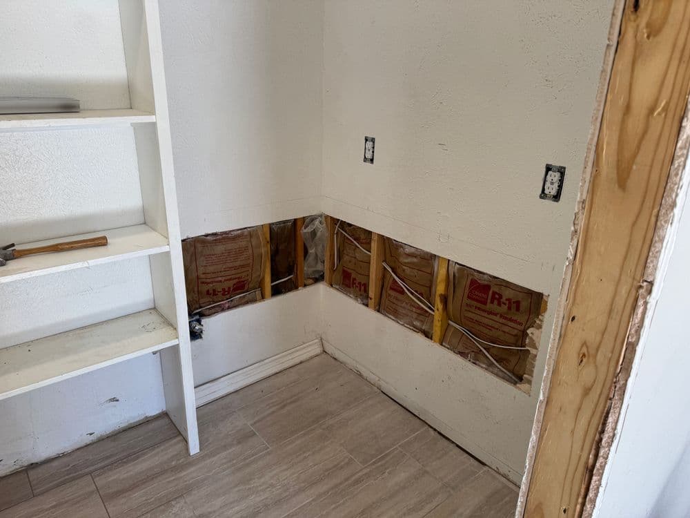 Drywall removed in corner room, showing R-1 insulation and electrical outlets. Home renovation project.