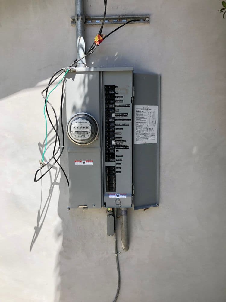 Electrical panel with connected meter and wires on a gray wall.