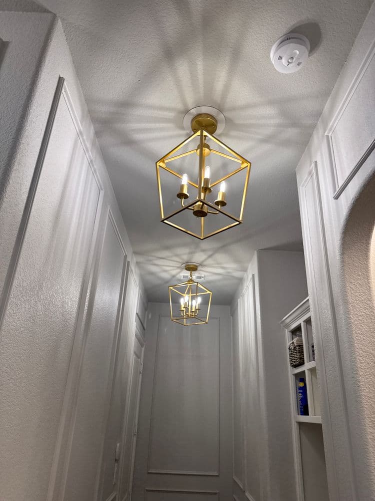 Elegant hallway featuring two gold pendant lights casting intricate shadows on white walls.