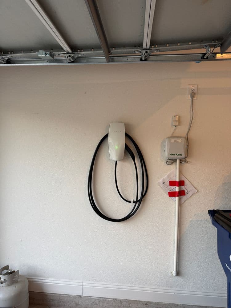 Tesla wall charger installed in a garage with coiled charging cable and utility panel.