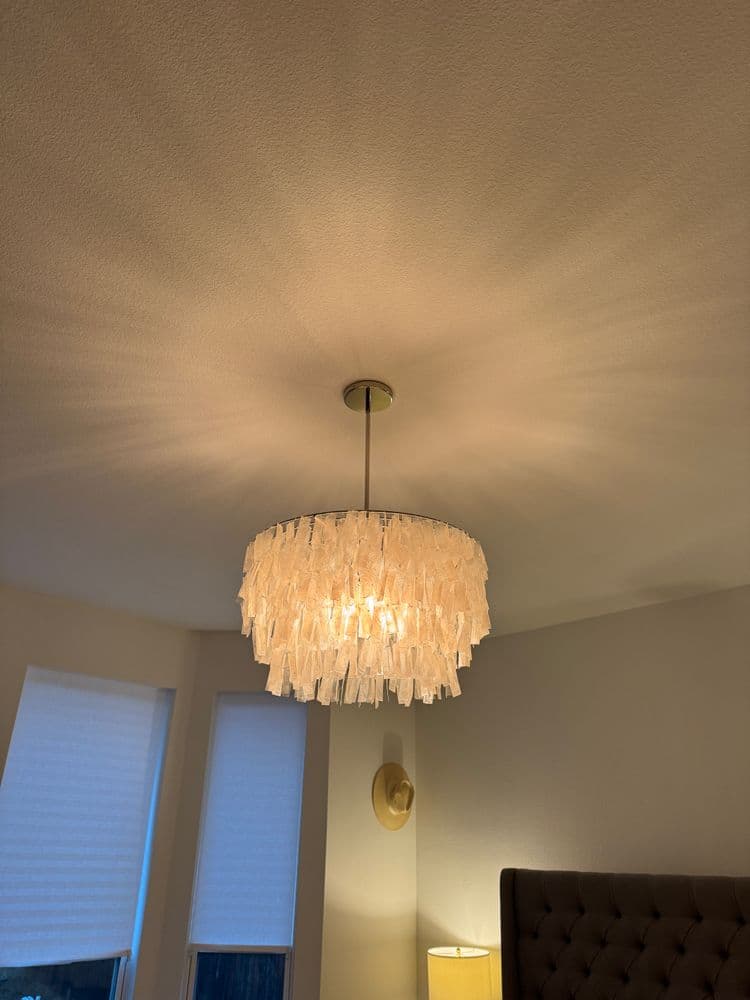 Modern chandelier with fringed design illuminating a cozy bedroom setting.