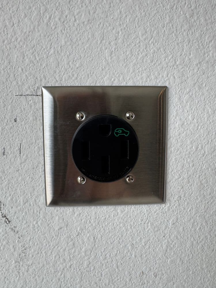 Electric vehicle charging outlet mounted on a wall, featuring a green indicator light.