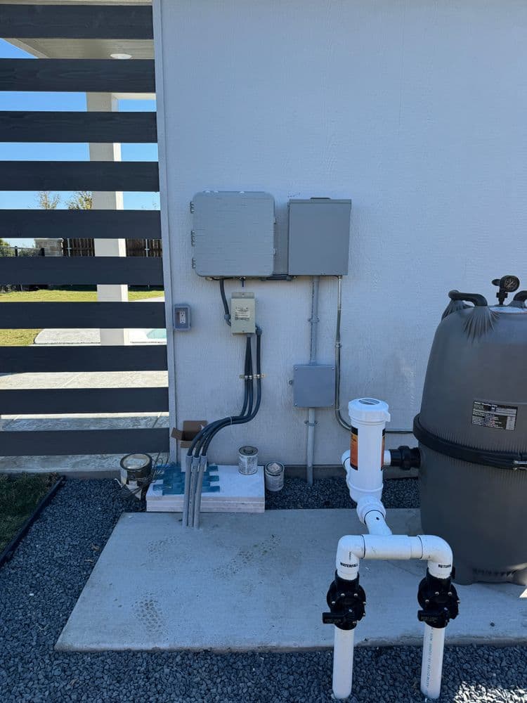 Pool equipment setup with pipes, electrical box, and filter near a modern fence.