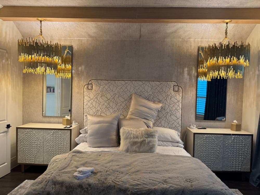 Elegant bedroom with gold chandeliers, plush bedding, and stylish decor accents.