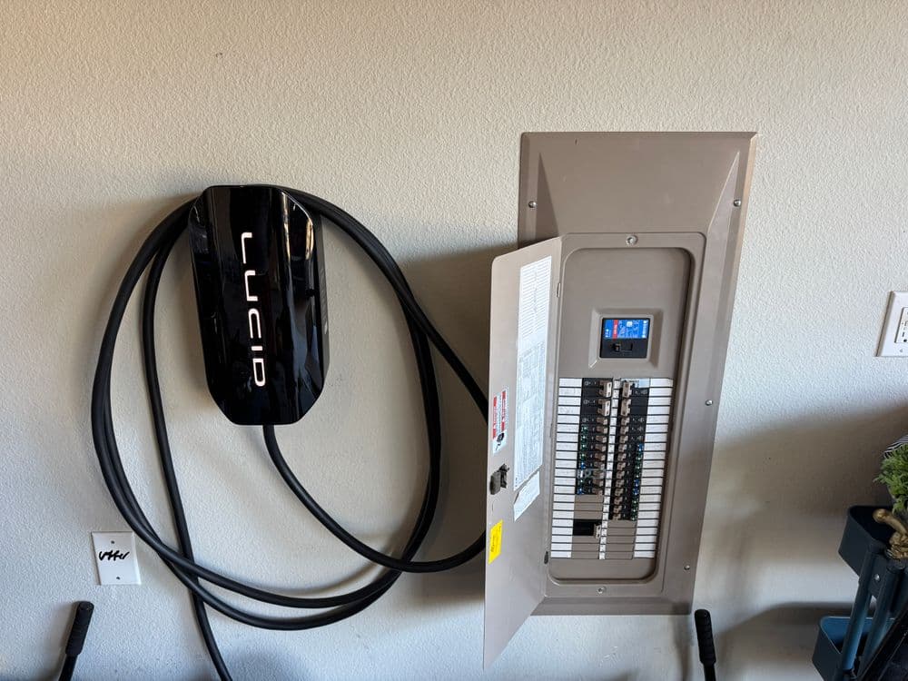 Lucid electric vehicle charger mounted on a wall, next to an open electrical panel.