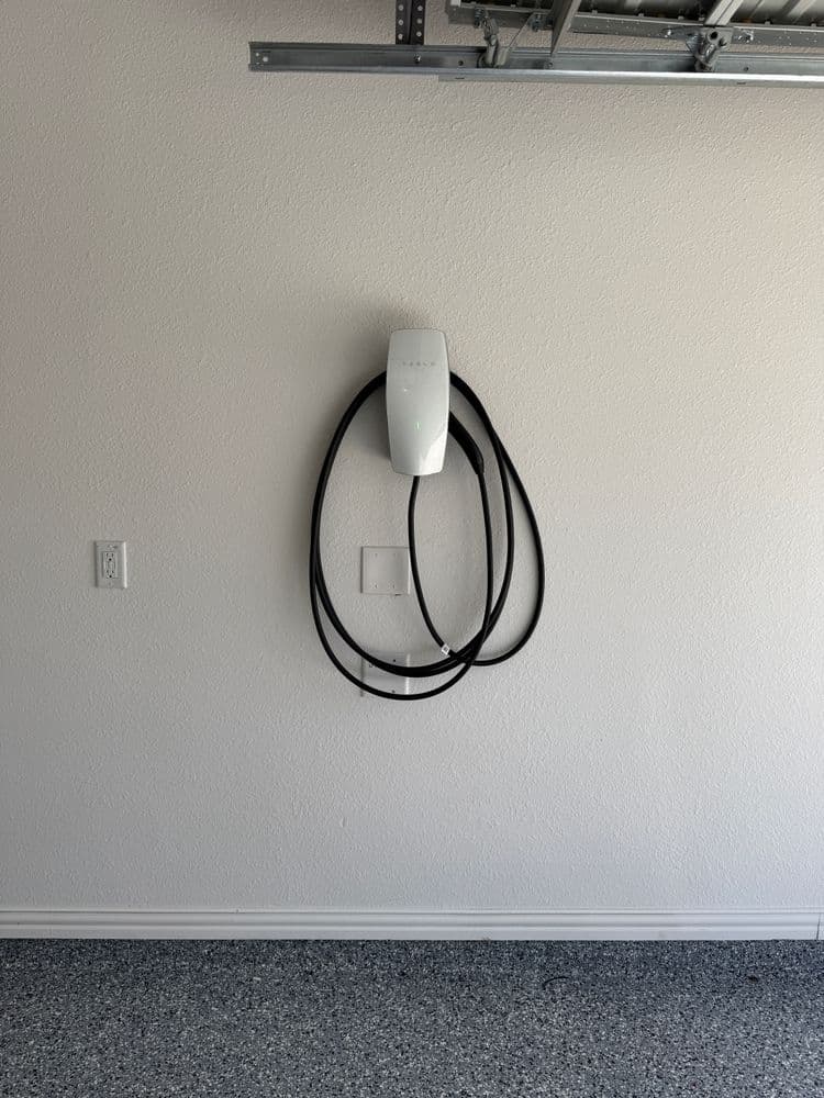 Tesla wall connector installed in a garage, with charging cable neatly coiled.