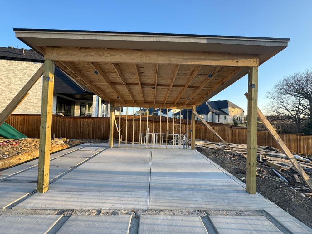 Outdoor patio construction with wooden framework and concrete flooring behind a house.