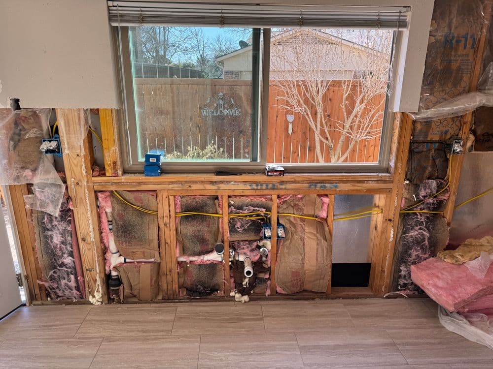 Exposed wall during home renovation showing insulation, plumbing, and electrical work.