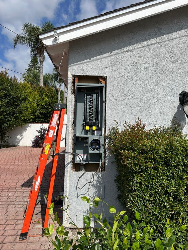Electrical panel installation with ladder beside residential home in sunny outdoor setting.