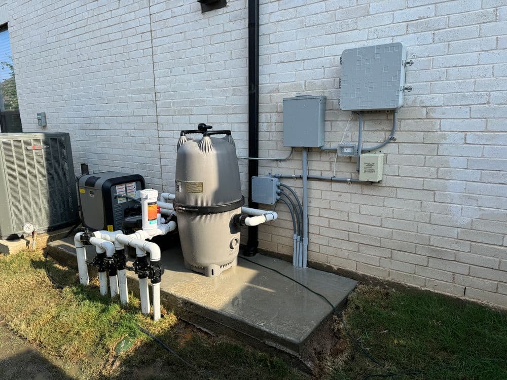 Pool pump and filtration system outside a home, with adjacent electrical panel and plumbing.
