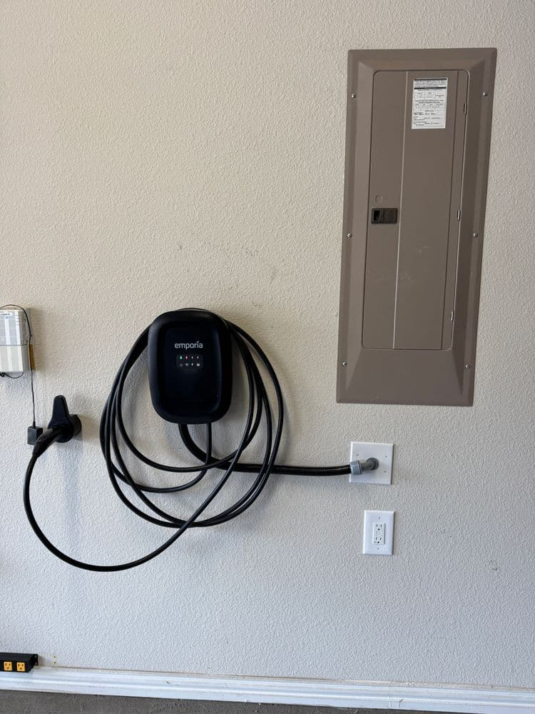 Electrical panel and Emporia EV charger mounted on garage wall with charging cable.