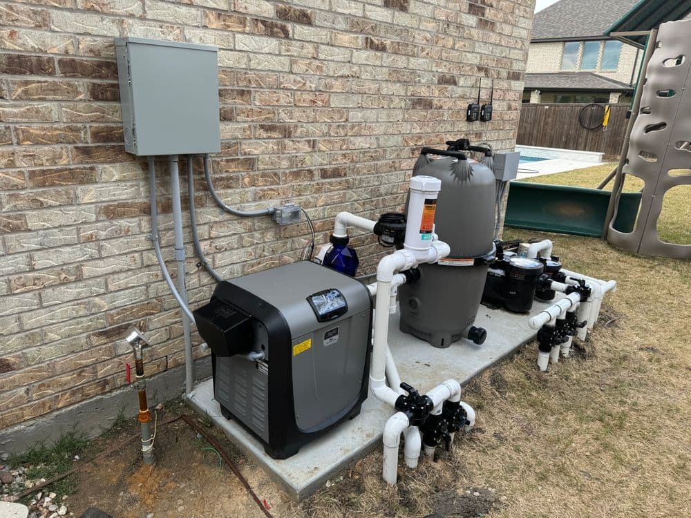 Pool equipment setup with heater, filter, and plumbing installed on a brick wall.