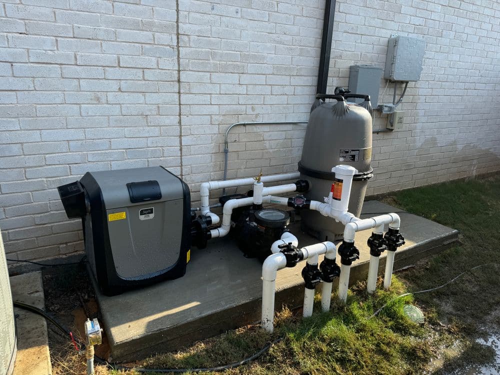 Residential pool filtration system with pump, heater, and plumbing on a concrete slab.
