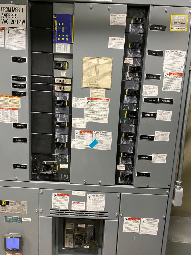 Electrical panel with circuit breakers and safety labels in a commercial setting.