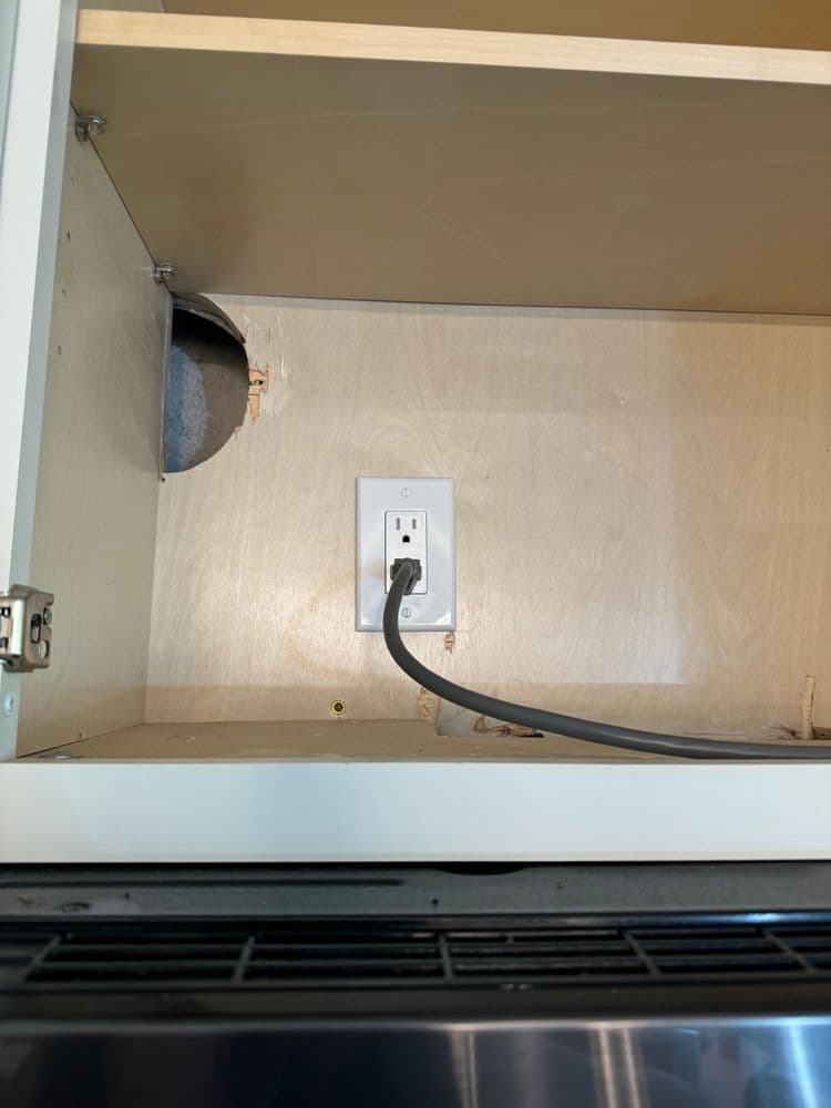 Electrical outlet inside kitchen cabinet with power cable visible, showcasing installation details.