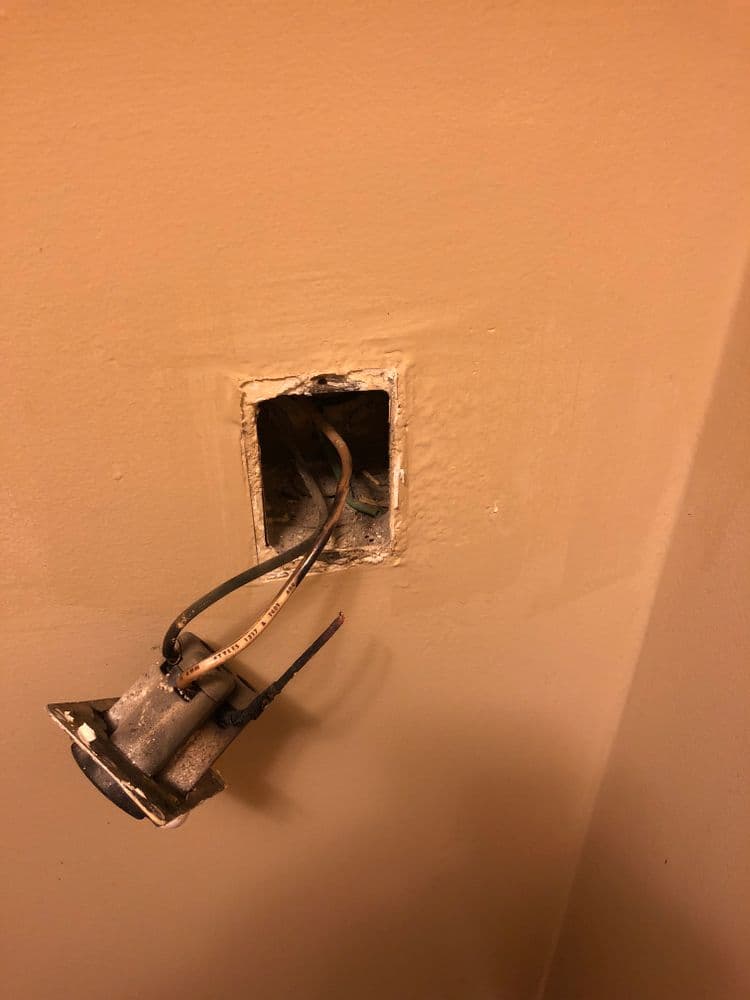 Electrical outlet box with exposed wires on a wall showing potential repair needs.