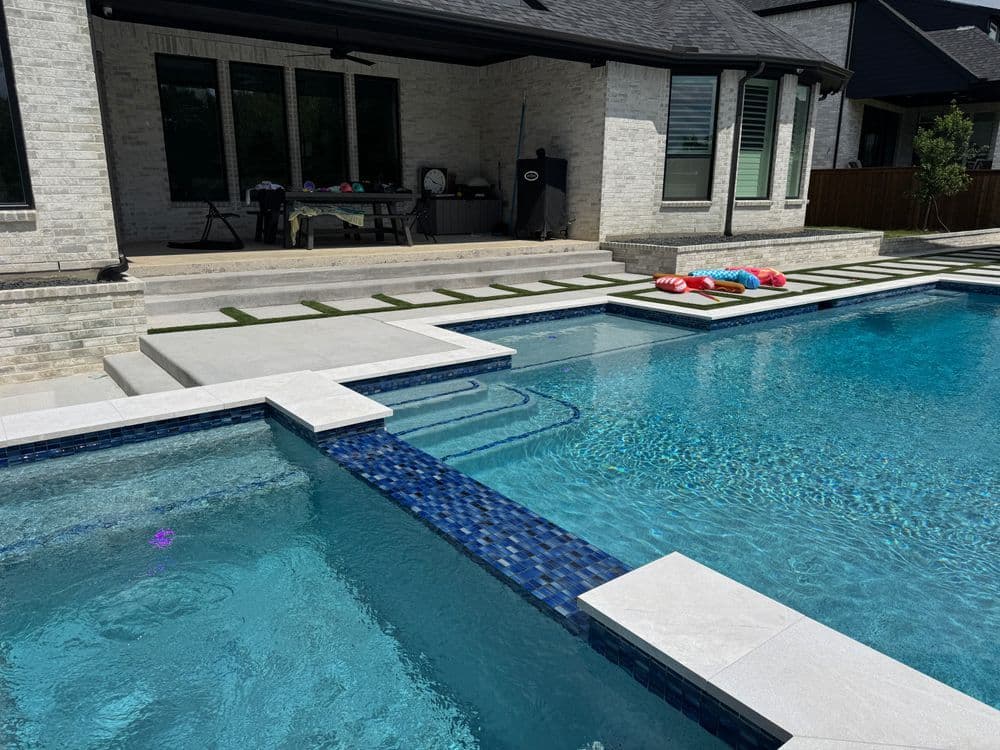 Modern backyard pool with clear water, stone patio, and lounge area, ideal for relaxation.