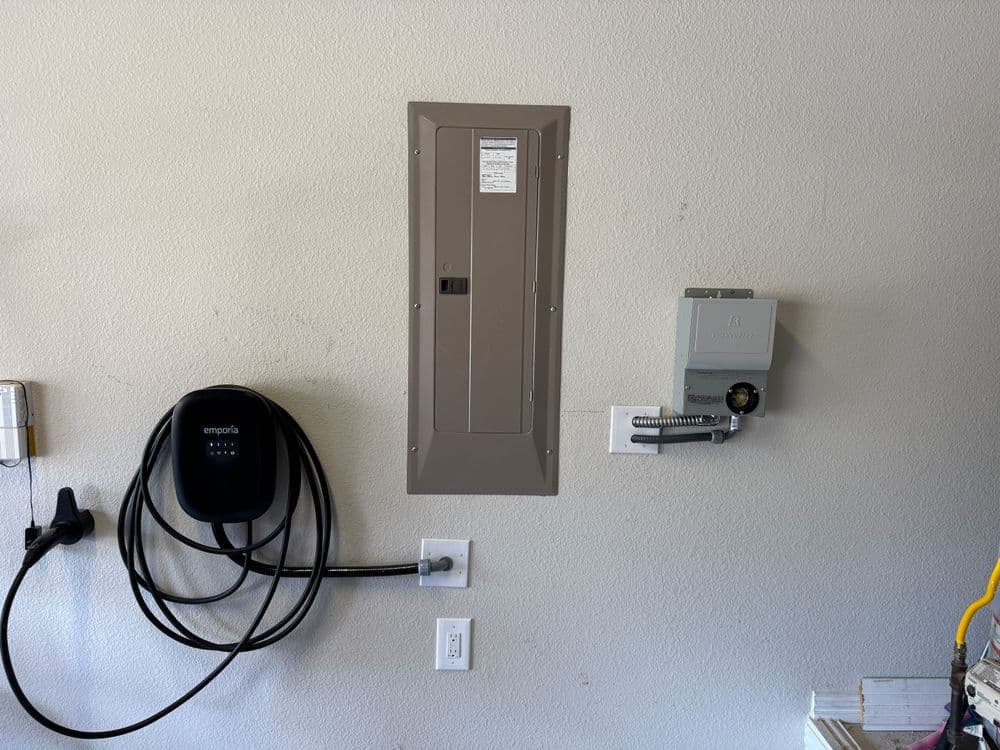 Home charging station for electric vehicle and electrical panel mounted on garage wall.