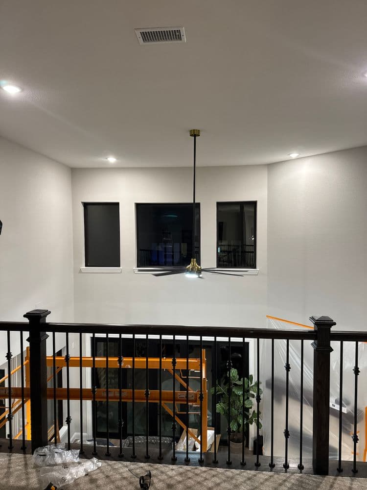 Modern home interior featuring a stylish ceiling fan, large windows, and wood railing.